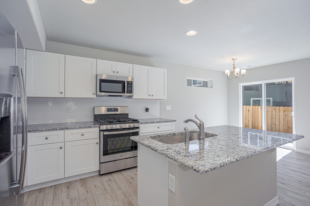 Angled kitchen view featuring a granite island, sink, stove, microwave and a sliding door to a fenced yard.