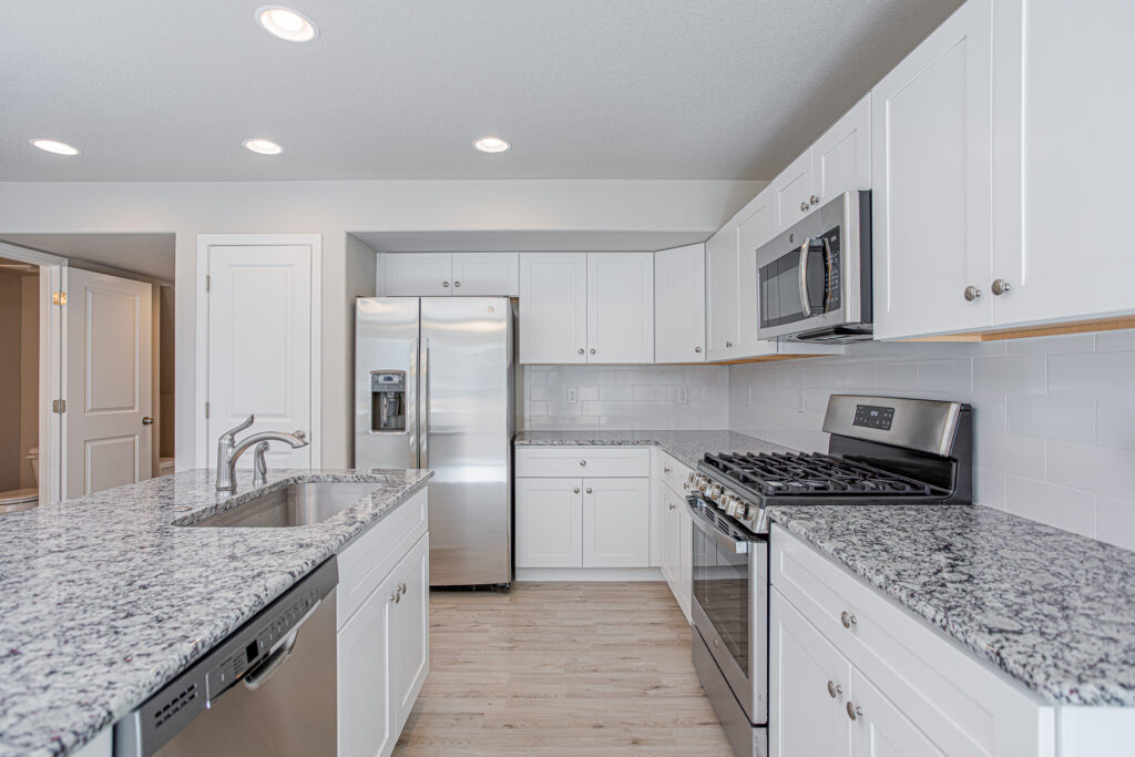 Bright modern kitchen with white cabinets, granite island, stainless appliances, and light wood flooring.