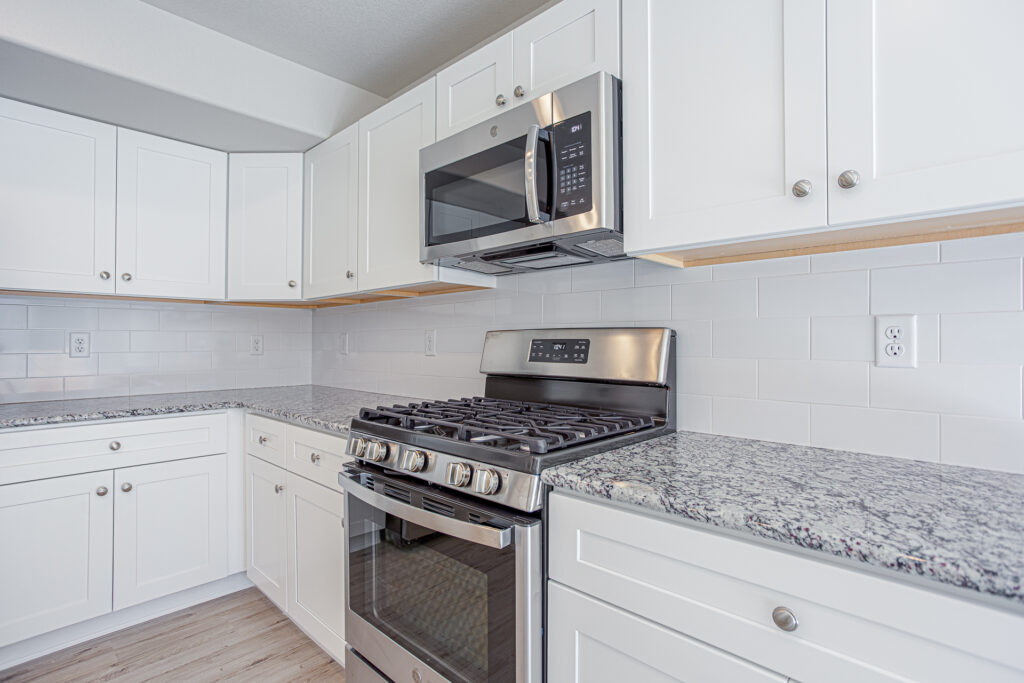 Close-up of stainless steel gas range and over-the-range microwave with white cabinetry and tiled backsplash.
