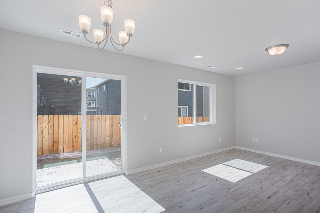 Empty bright living or dining area with sliding glass door, window, chandelier, and light wood-look flooring.