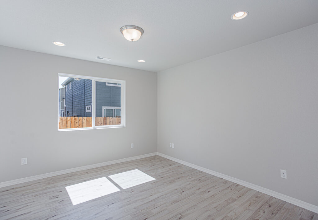 Empty room with light wood-look floor, single window, and ceiling lights casting sunlight on the floor.