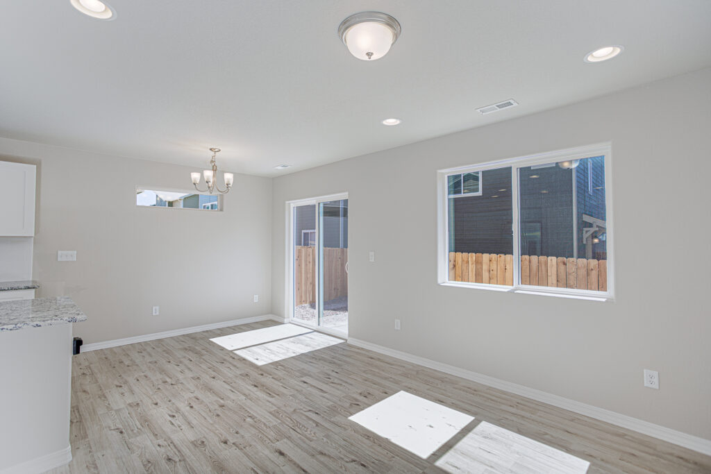 Open living area with sliding glass door, two windows, and light wood-look flooring.