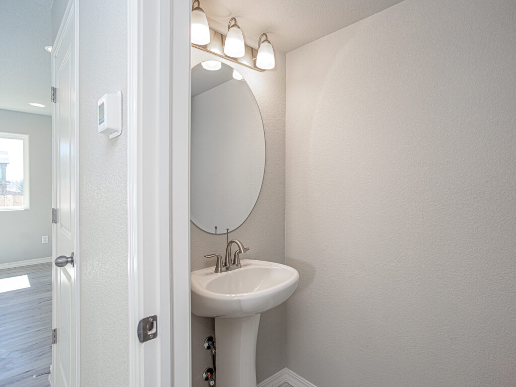 Small powder room with pedestal sink, oval mirror, and three-bulb vanity light.