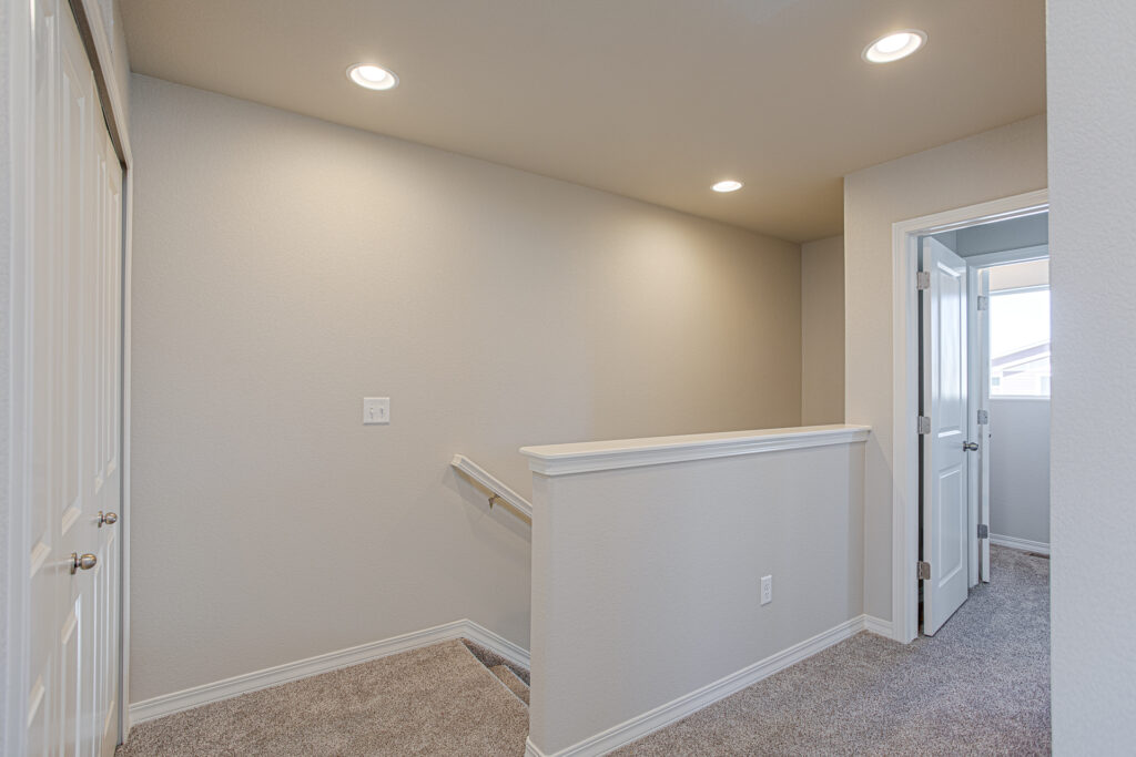 Upper landing with carpeted stairs, half wall railing, recessed ceiling lights, and doorway to a room.