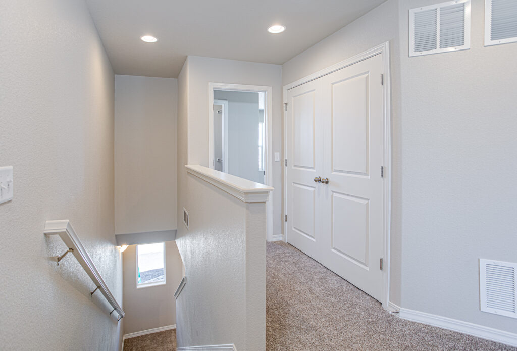 Carpeted upstairs landing with stairwell, double-door closet, and neutral painted walls.