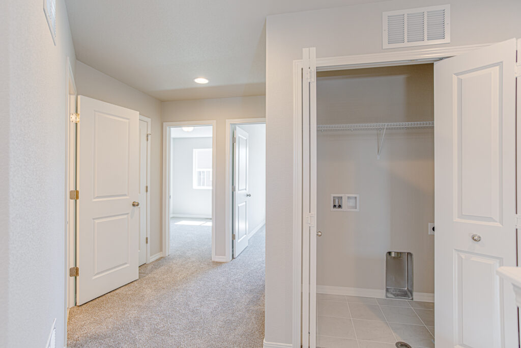 Hallway with open doors to rooms and a small laundry or utility closet with hookups.