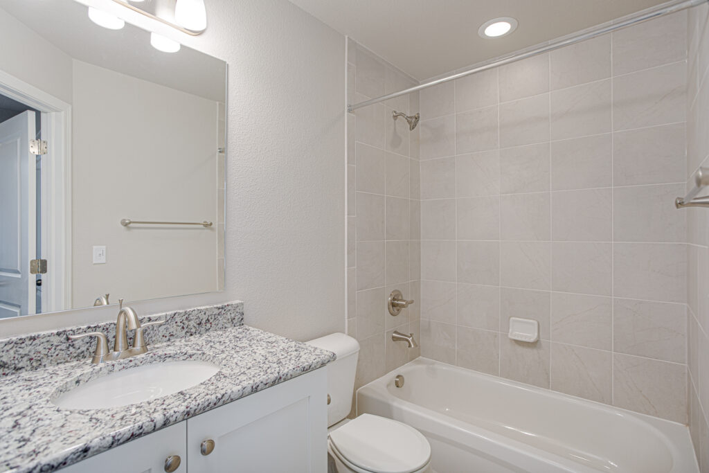 Bathroom with vanity, granite countertop, mirror, toilet, and tiled bathtub/shower surround.