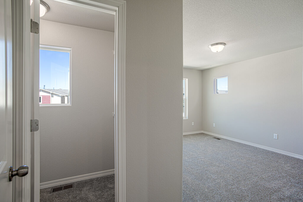 Room entry view into a carpeted bedroom with two small windows and adjacent closet doorway.