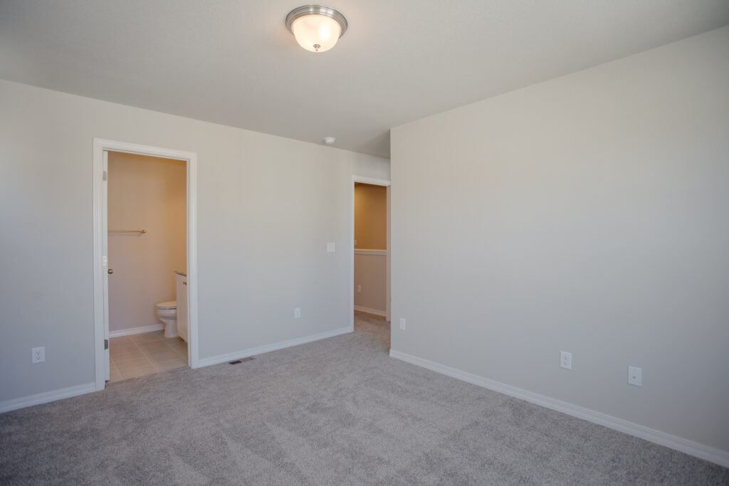 Empty bedroom with carpet, ceiling light, and a doorway leading to a small bathroom.