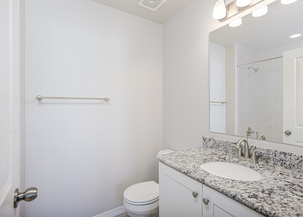 Small bathroom vanity with granite countertop, sink, mirror, and visible toilet.