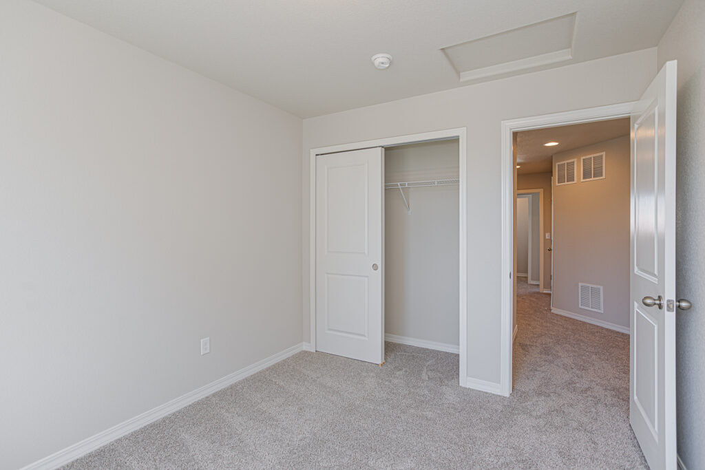 Small empty bedroom with carpet, open closet and doorway to a hallway, neutral paint.