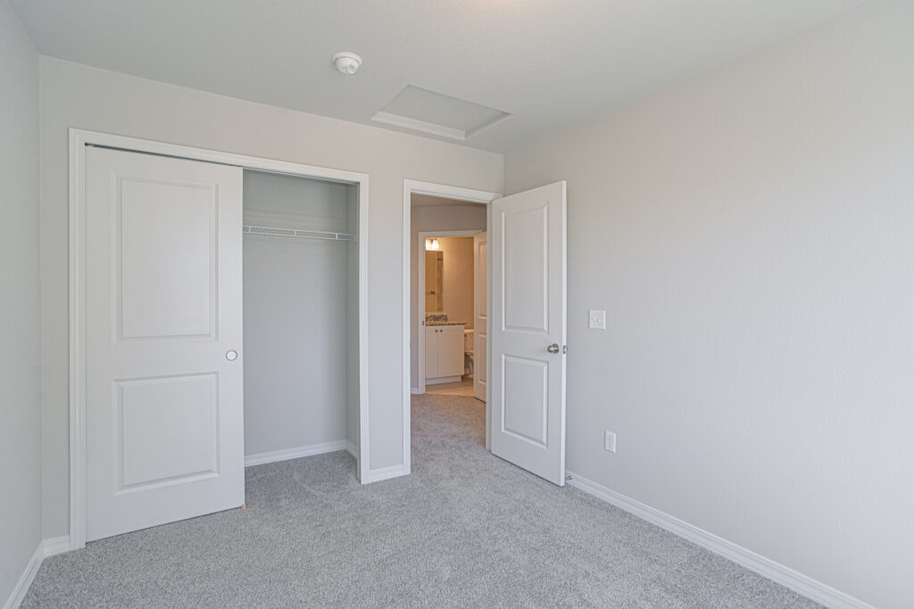 Empty bedroom view toward an open closet with sliding door and doorway to a bathroom area.