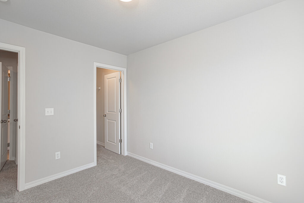 Neutral-tone empty bedroom with carpet and an open doorway to a closet or adjoining room.