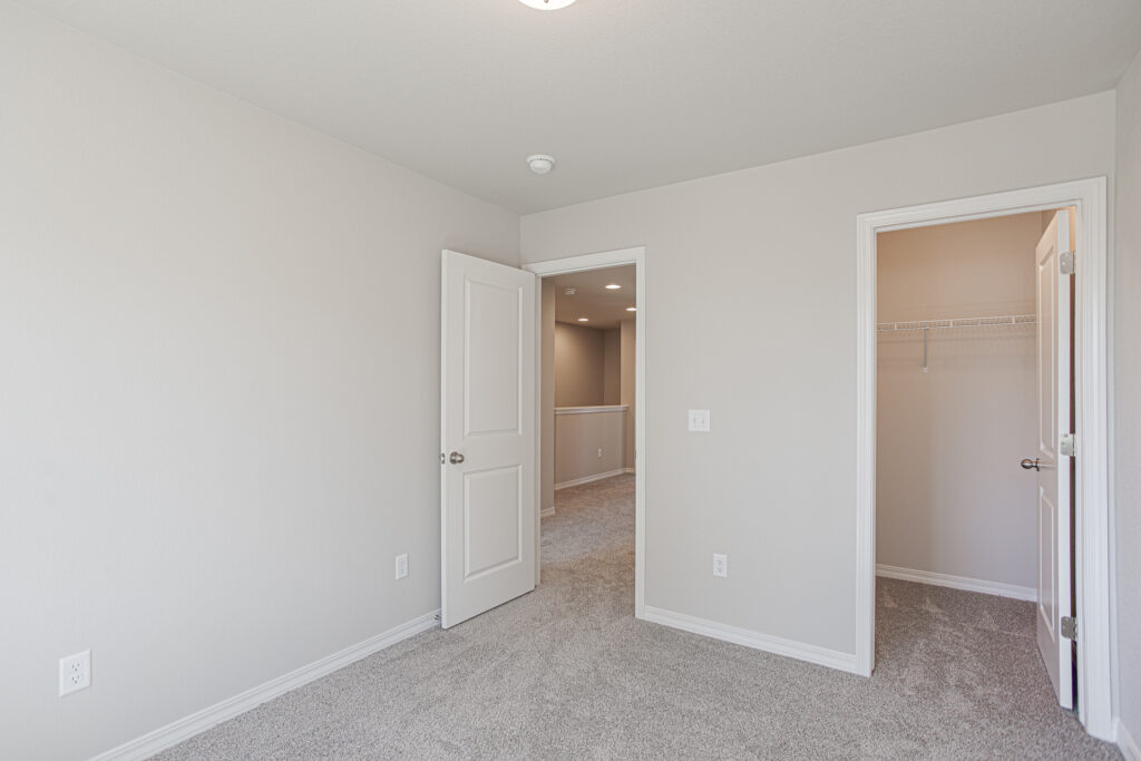 Empty carpeted bedroom with open door to hallway and doorway to a small walk-in closet.