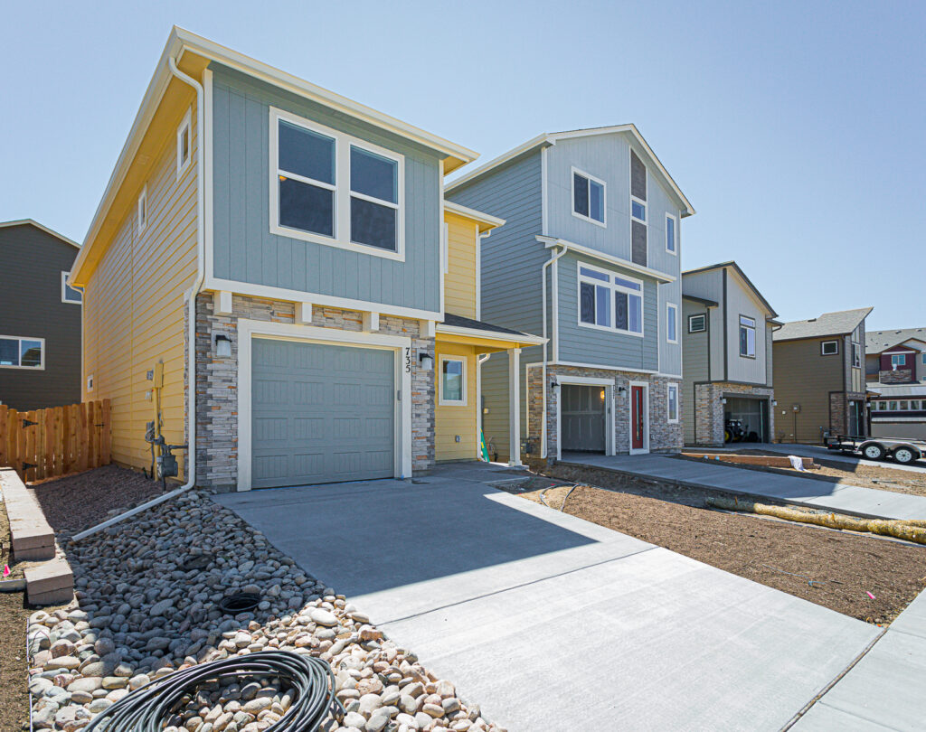 Street-facing new-construction houses with garages, light blue and yellow siding, and concrete driveways.