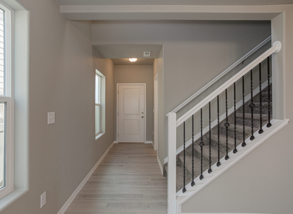 Interior entry hallway with white door, windows and carpeted staircase with black balusters.