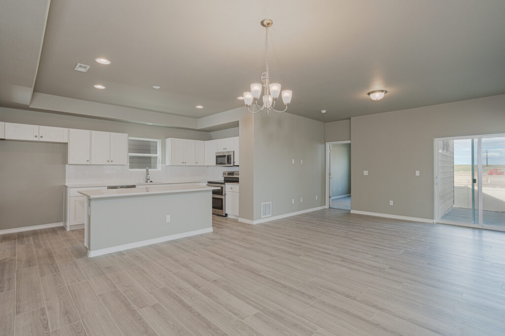 Open-plan living area with kitchen island, dining chandelier, and sliding glass door to the outside.