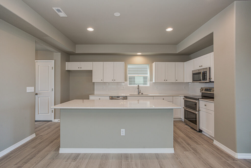 Straight-on view of a kitchen island with white cabinetry, quartz countertop, and window above the sink.