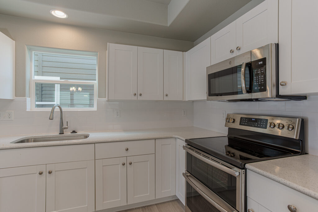 Close-up of a kitchen corner with white cabinets, sink, and stainless steel range and microwave.