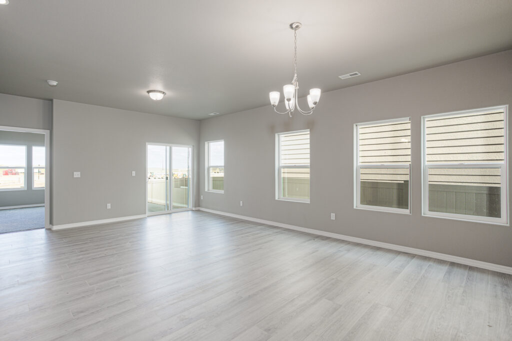 Bright open living area with light gray floors, multiple windows, and a central chandelier.