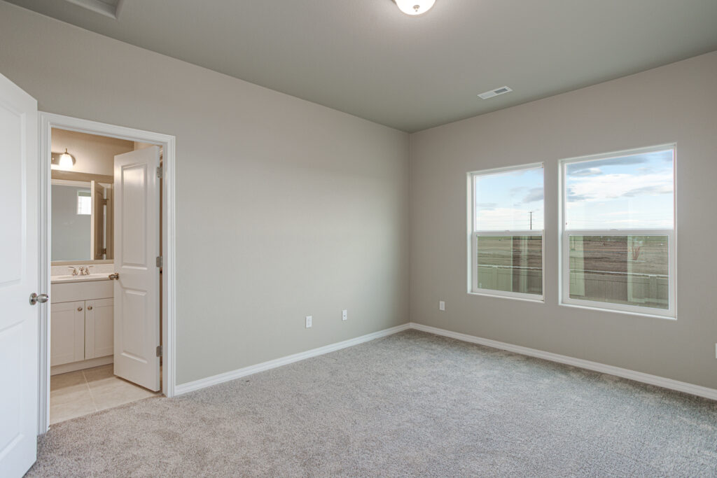 Carpeted bedroom with en-suite bathroom doorway and two side-by-side windows.