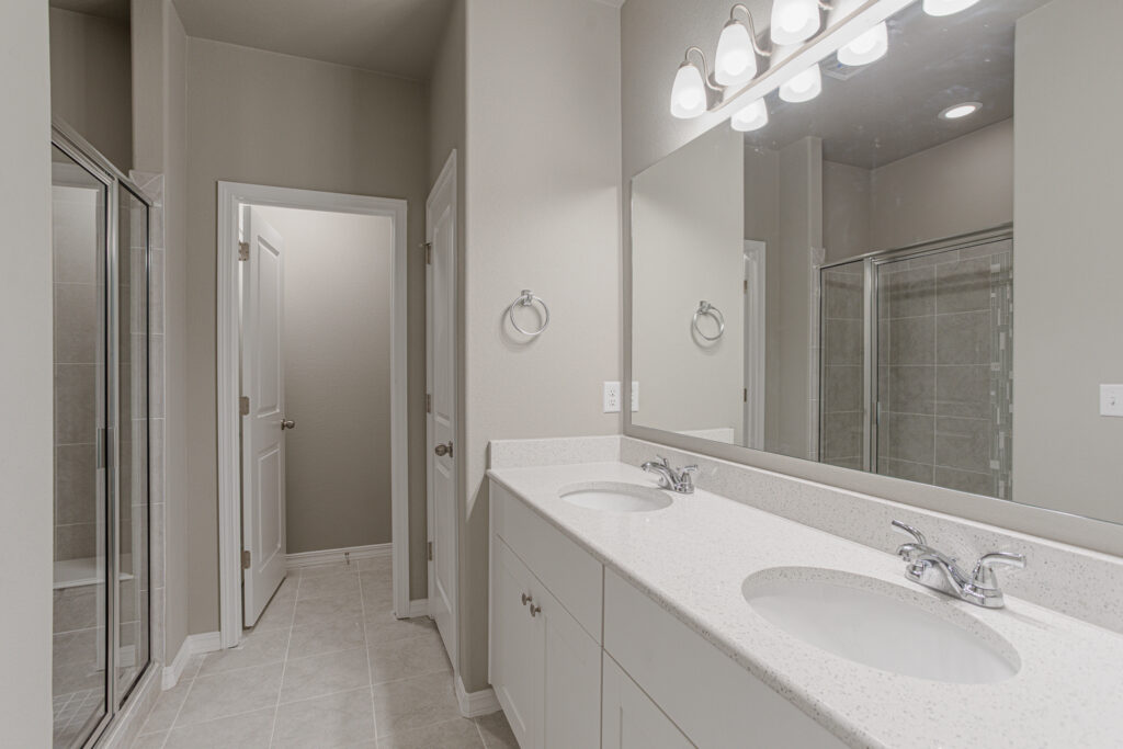 Neutral-toned bathroom with double sink vanity, large mirror, and tiled walk-in shower.