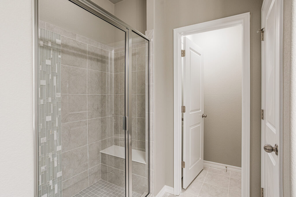 Tiled shower with glass sliding door and built-in bench next to a doorway.
