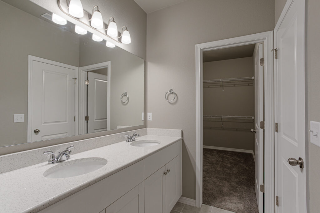 Bathroom vanity with two sinks, wide mirror, and an open door revealing a closet.
