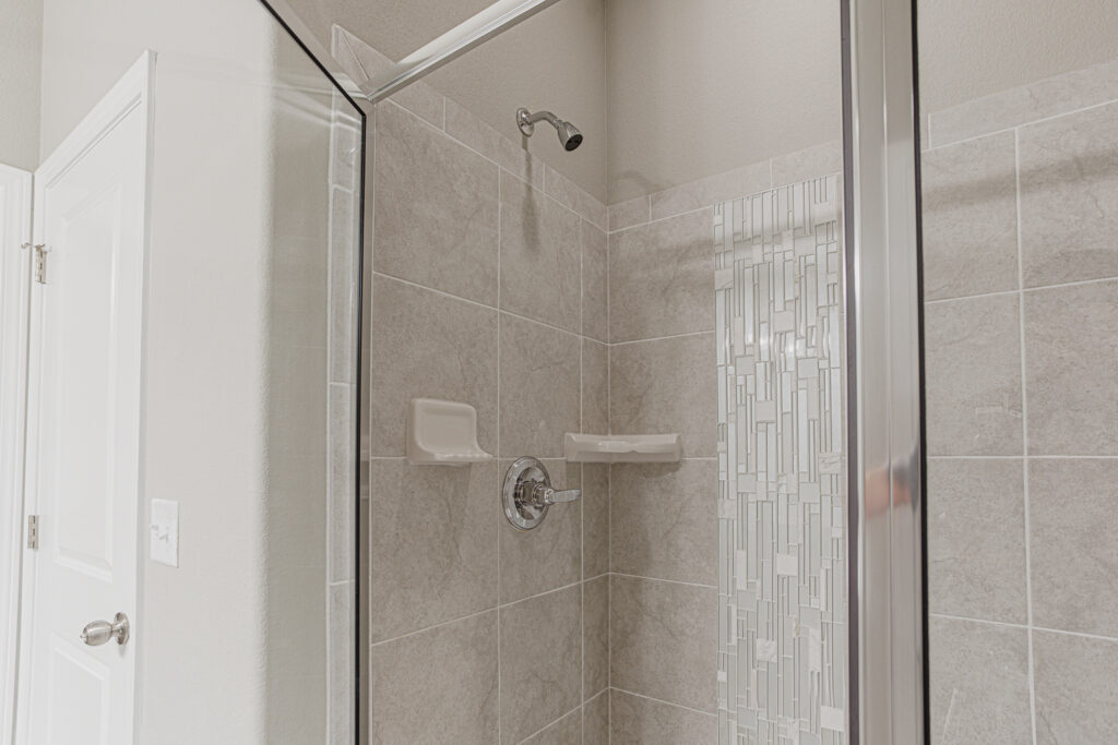Tiled walk-in shower with glass door, built-in soap dishes, and vertical mosaic accent strip.