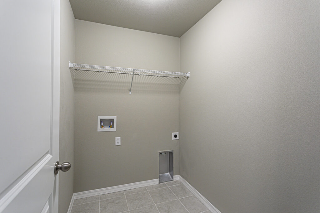 Small laundry or utility room with tiled floor, wall shelf and washer/dryer hookups.