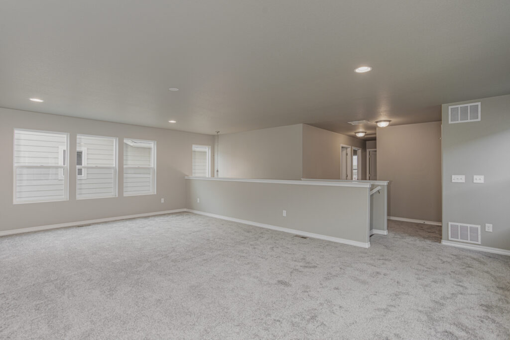 Large open carpeted living area with half wall and multiple windows along one side.