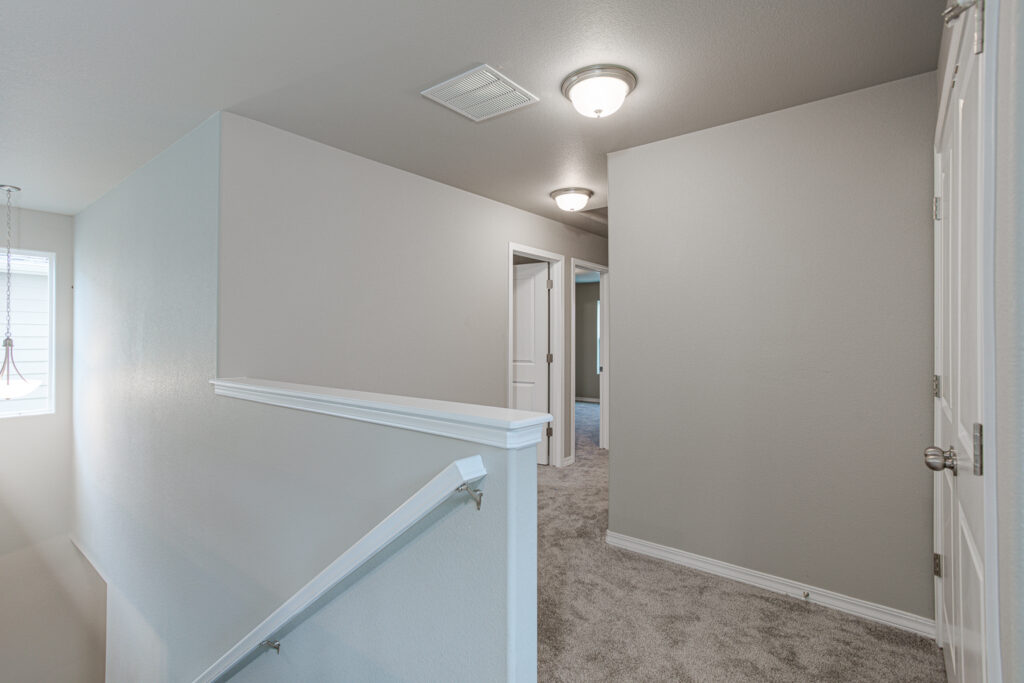 Upstairs hallway landing with carpet, half wall railing and two ceiling lights.