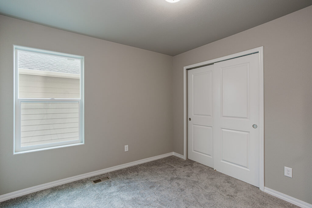Bedroom with window on left and closet with sliding white doors on right.