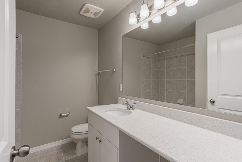 Bathroom vanity with sink, large mirror, toilet and tiled shower in reflection.
