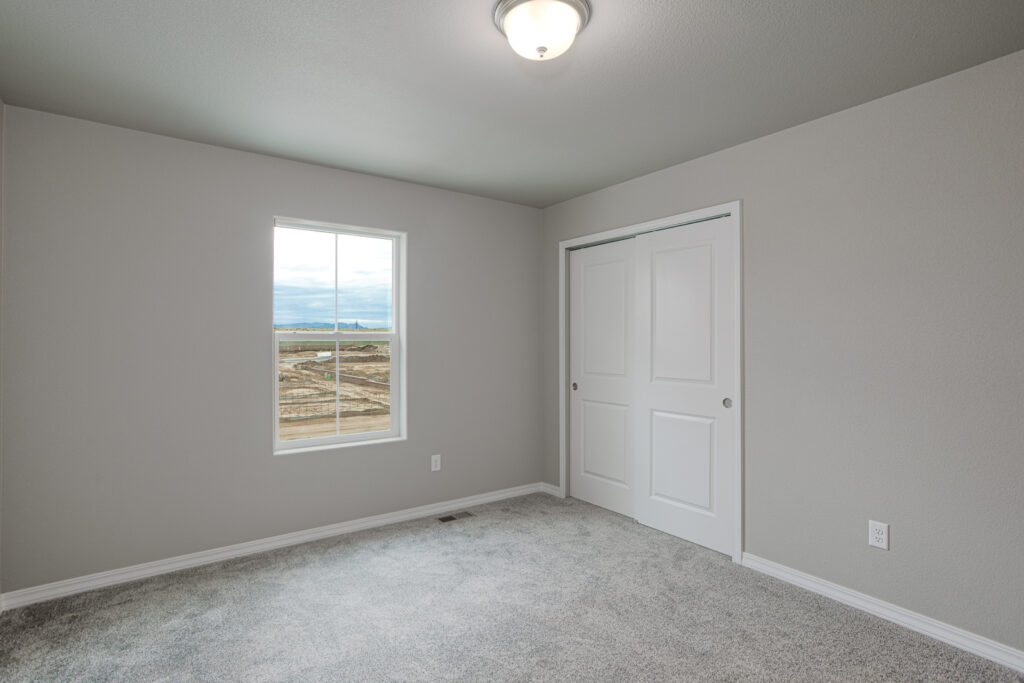 Small empty bedroom with closet doors, carpet, window, and ceiling light.