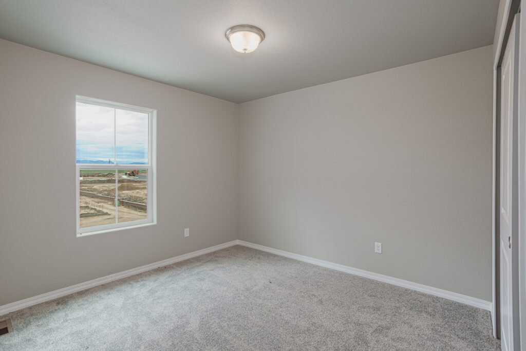 Small empty room with gray carpet, single window and neutral painted walls.