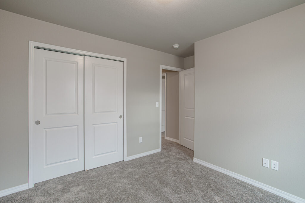 Empty room interior showing white double closet doors and an open doorway.