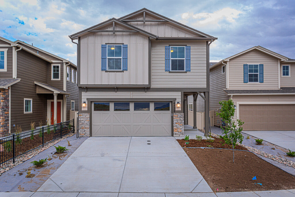 Completed two-story home with mixed siding, stone accents, blue shutters, and a concrete driveway.