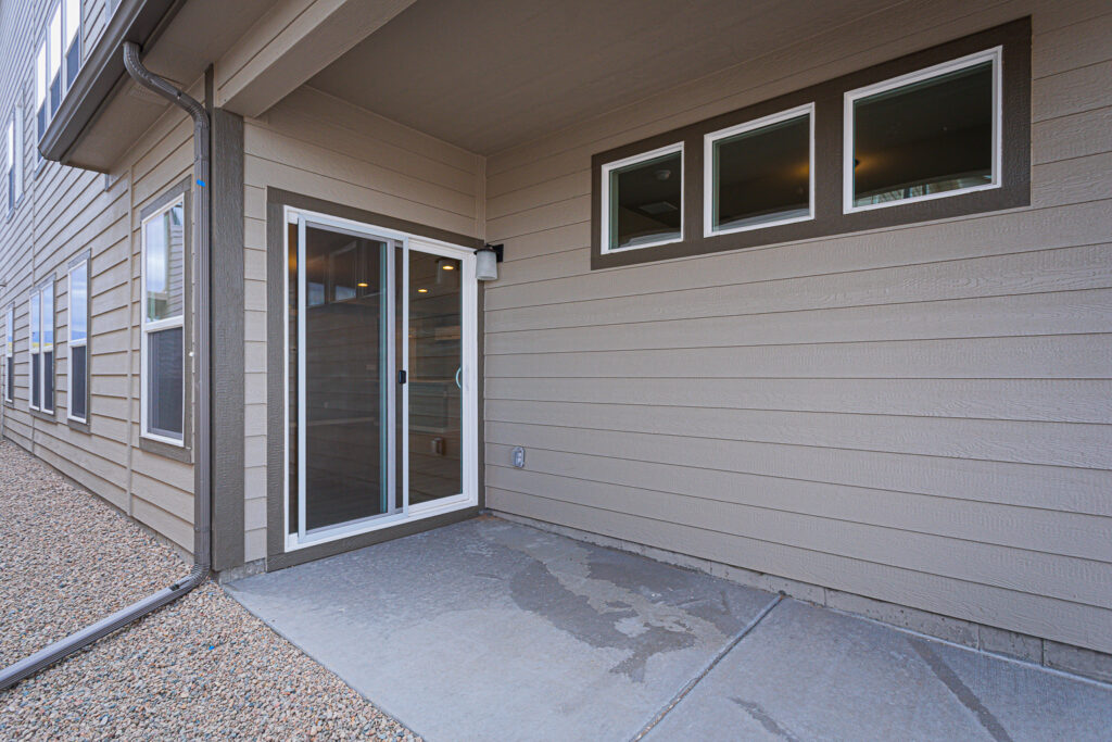 Covered concrete patio with sliding glass door and three small high windows on beige siding.