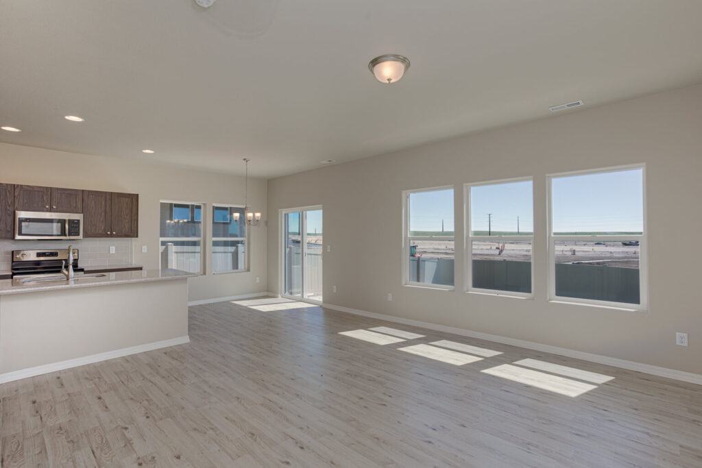 Bright open-plan living area with large windows, light wood flooring, and an adjacent kitchen.