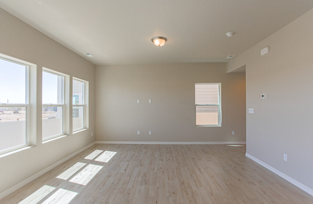 Empty bright room with three large side-by-side windows and pale wood flooring.