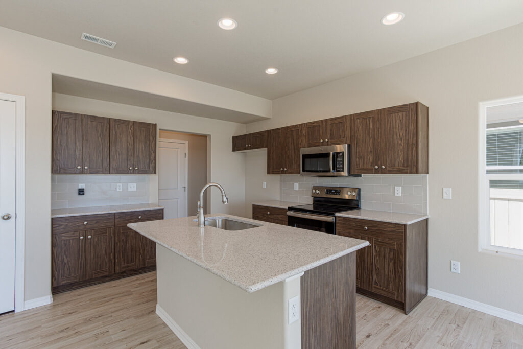 Kitchen view centered on island with sink, wood-tone cabinets and stainless appliances.