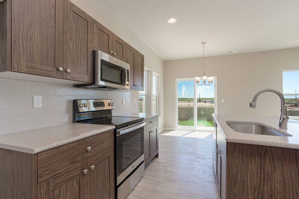 Kitchen perspective along counters with oven, microwave and island sink near sliding door.
