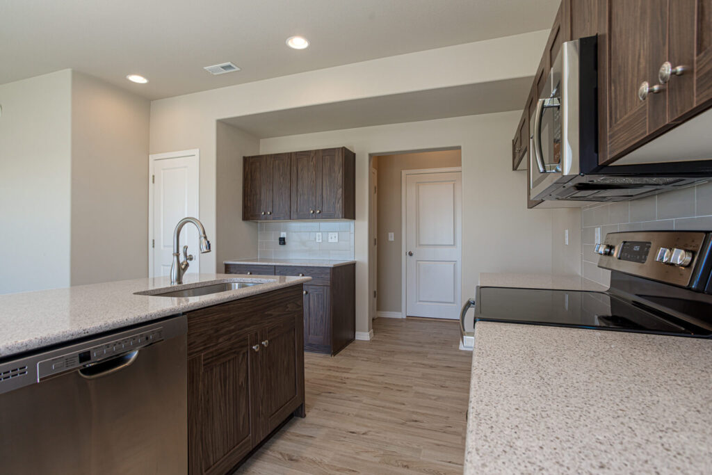 Modern kitchen island with sink, dark wood cabinets, stainless dishwasher and light wood flooring.