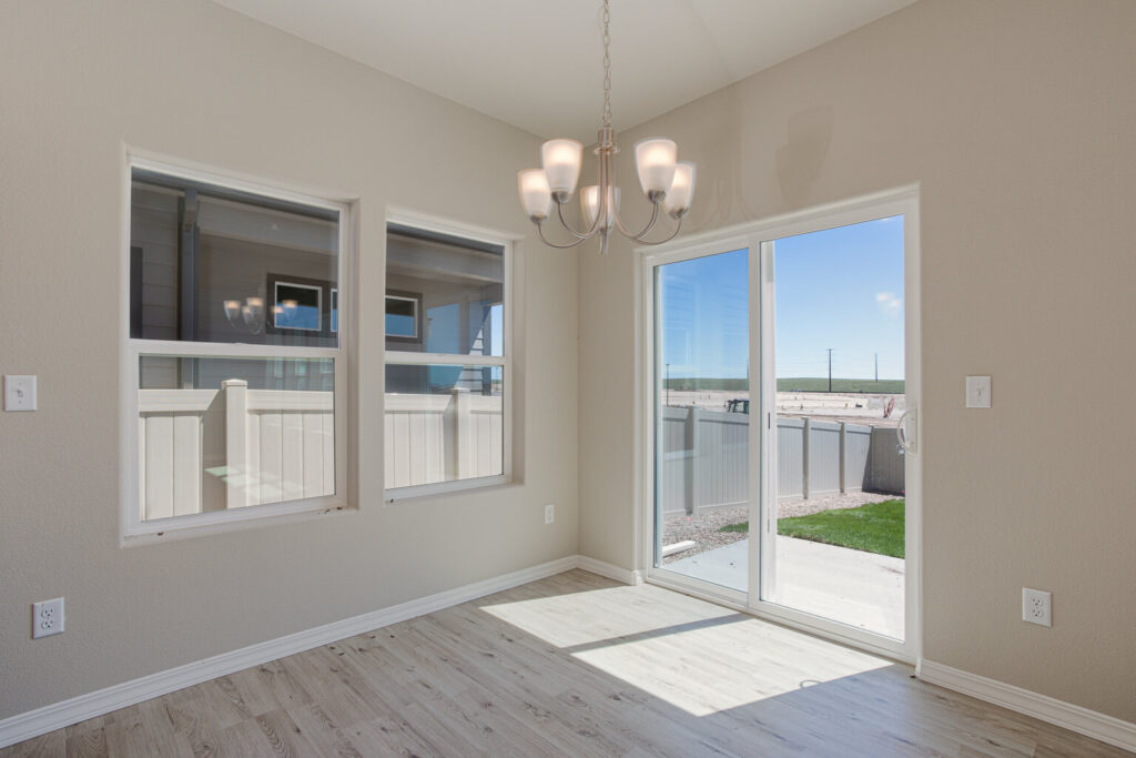 Bright dining nook with chandelier, two windows and sliding glass door opening to a fenced yard.