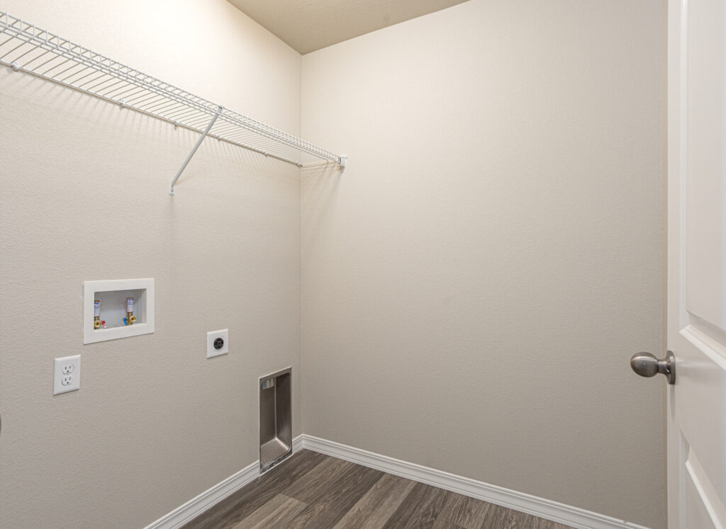 Laundry room with wire shelf, hookups for washer and dryer and a recessed dryer vent opening.