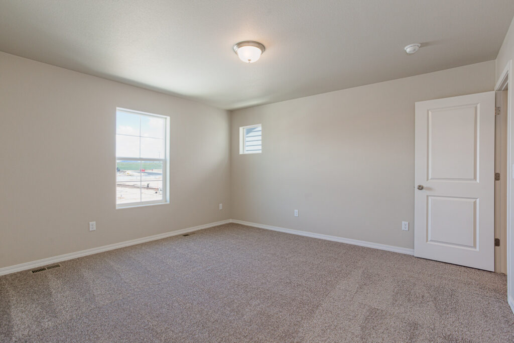 Spacious empty bedroom with two windows and light carpet under a central ceiling light.