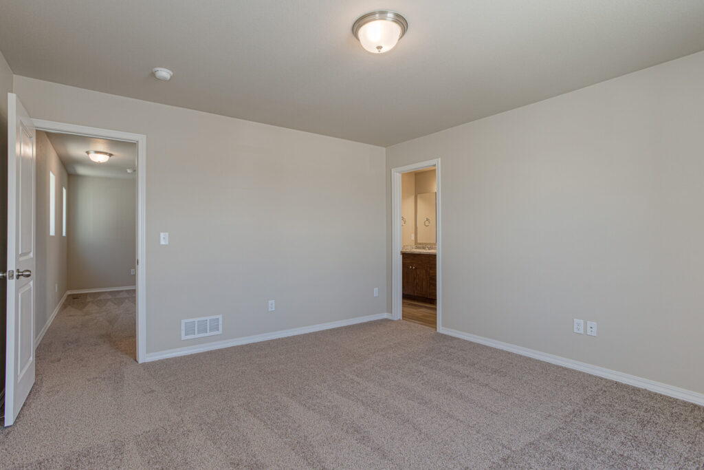 Carpeted bedroom facing a hallway and an open door revealing a bathroom vanity.