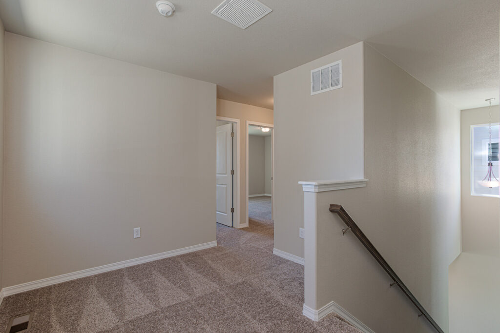 Small upstairs landing with carpeted floor, partial stair railing, and doorway to adjoining rooms.