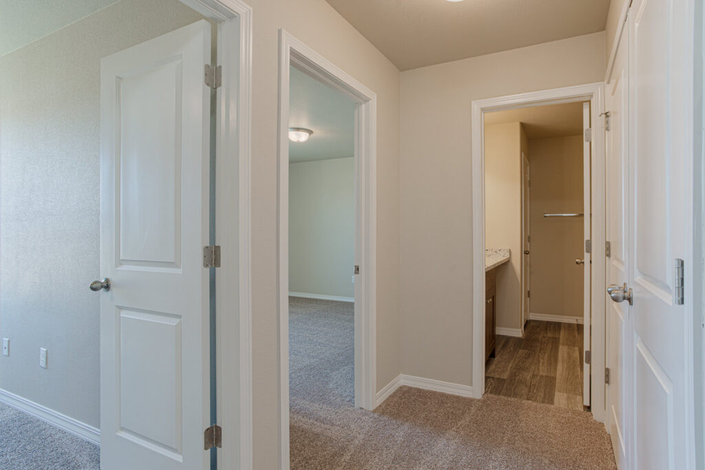 Hallway with open doorways to bedrooms and a bathroom, carpeted floors and white doors.